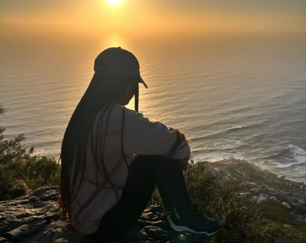 Awoman sitting on a mountain overlooking the sunset and ocean