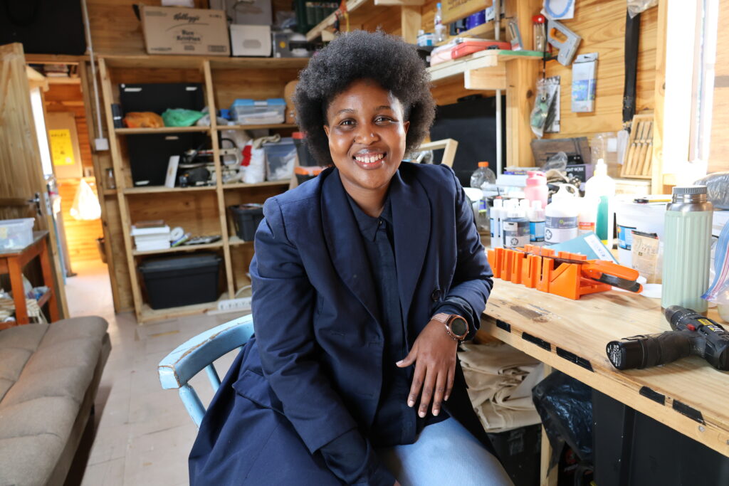 A woman poses in front of a workshop desk with equipment around her