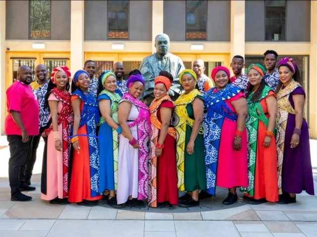 A group of people in a choir pose together wearing colourful clothing in front of a building